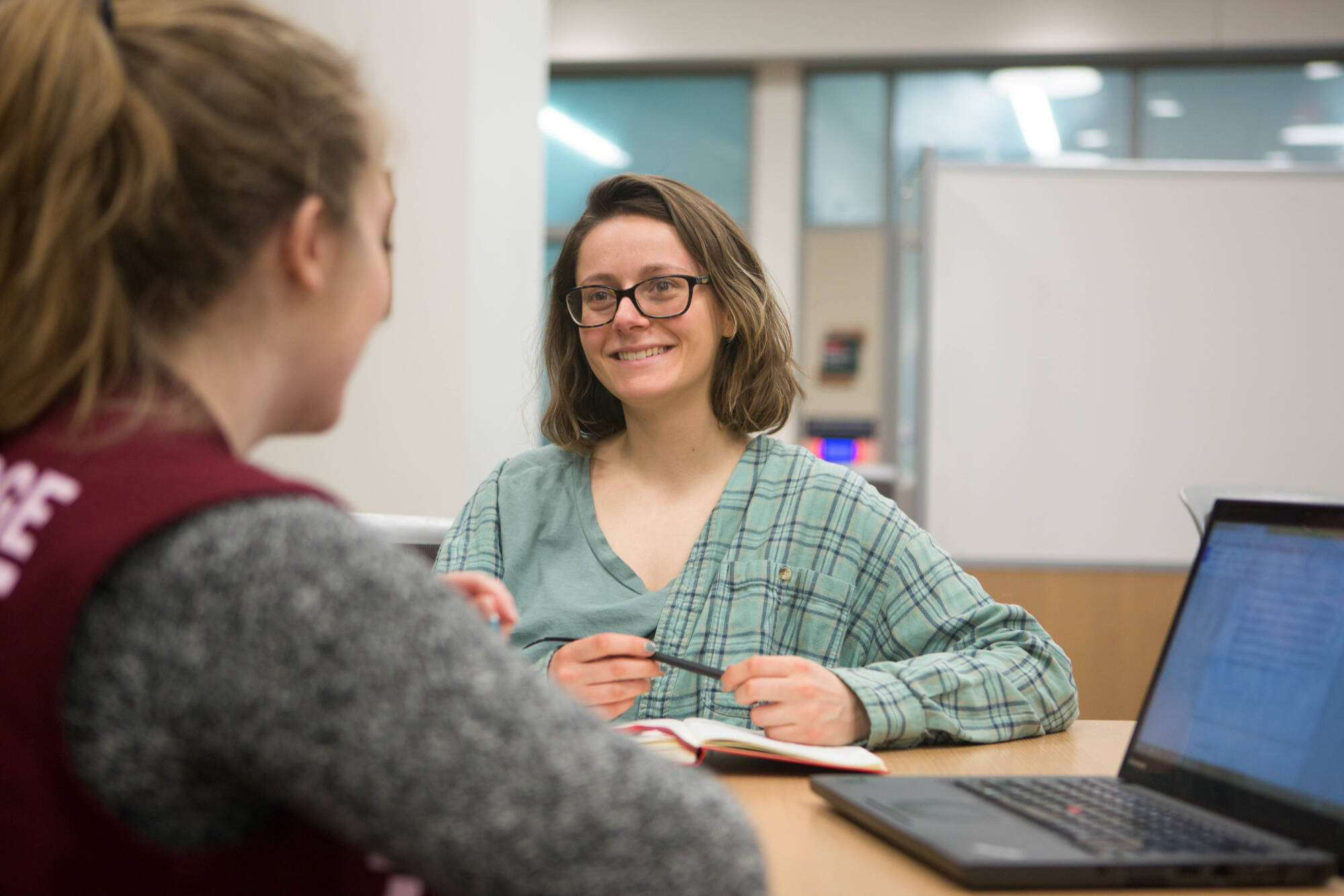 Two people sitting at a table, one facing the camera and smiling with a pen and notebook.